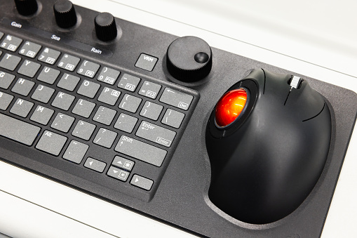 Built-in tabletop input device, black industrial keyboard with red trackball mouse, modern navigation equipment mounted on a control panel at captains bridge