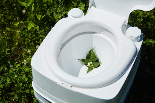White plastic toilet with an open lid. It stands on the green grass in the garden. The concept of recyclable raw materials and an environmental solution for nature pollution.