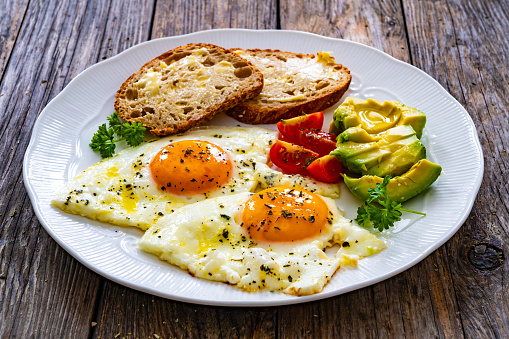 Continental breakfast -   fried eggs with fresh avocado and tomatoes on wooden table