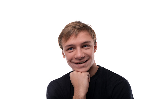 Positive Caucasian fair-haired teenager guy smiling at the camera on a studio background.