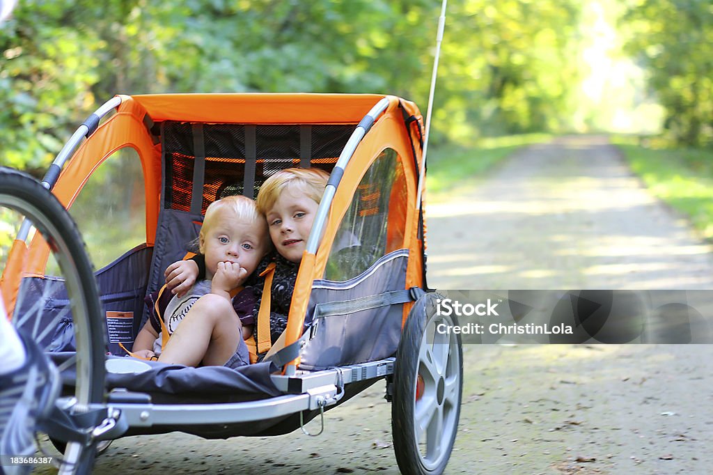 Two Boys in Bike Trailer Outside Two young children are sitting together in a pull behind bicycle trailer as they ride down a bike trail in the woods Bicycle Stock Photo