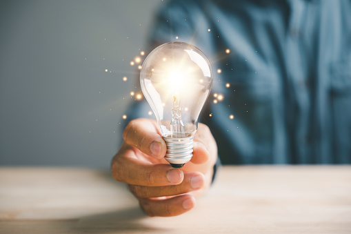 A man's hand gripping a light bulb, symbolizing the convergence of creative thinking, innovation, and solution-oriented approaches. This image portrays the essence of intelligent business success.