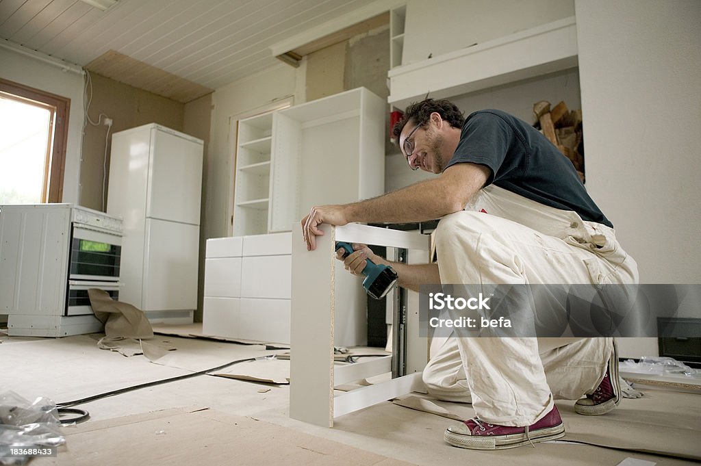 Assembling kitchen units. Man assembles kitchen units from packages. The packages come from furniture stores and must be assembled by the buyer. This concept contributes to cost savings for the buyer Adult Stock Photo