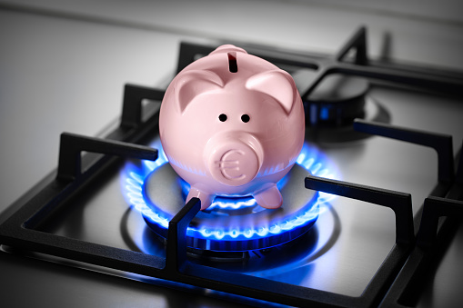 Piggy bank with euro symbol on a range burner of a natural gas home stove surrounded by a blue flame.