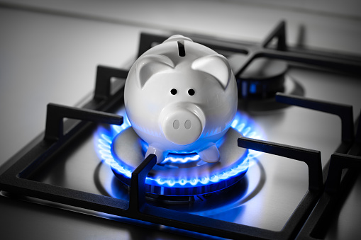 Piggy bank on a range burner of a natural gas home stove surrounded by a blue flame.