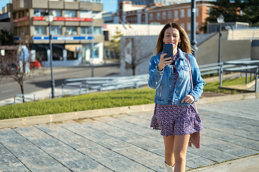 Young Woman Reading A Message On The Phone While Walking In The City