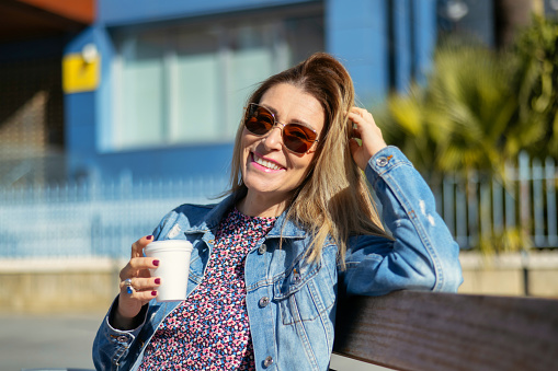 Smiling Young Woman With Positive Emotion Having Coffee Outdoors. Businesswoman Outside Work Building Taking A Break.