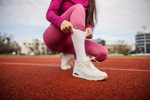 Cropped picture of a sportswoman adjusting her sock and preparing for exercise on stadium.