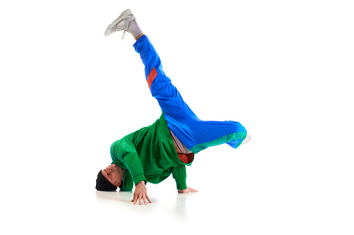 Stylishly dressed man performing freestyle, breakdance, standing on hands raised up legs against white background. Swipe. Concept of action, art, beauty, sport, youth. Dancer shows breakdance figures