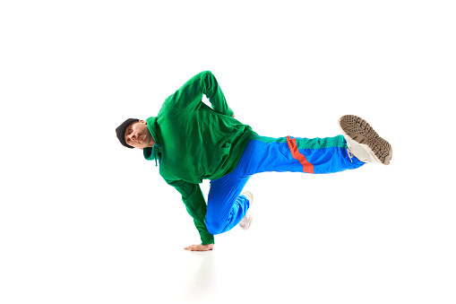 Young athletic man, b-boy dancing hip-hop, breakdance on one hand raising legs up in motion against white background. Concept of action, art, beauty, sport, youth. Dancer shows breakdance figures