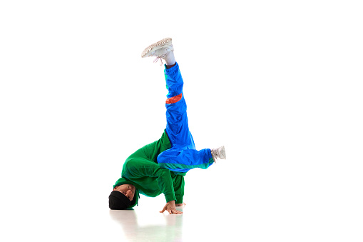 Young flexible sportive man dancing freestyle dance in green and blue sport uniform against white studio background. Concept of action, art, beauty, sport, youth. Dancer shows breakdance figures