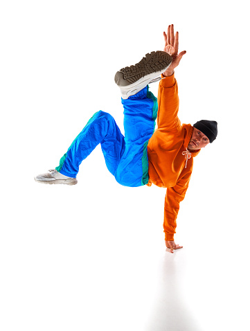 Stylishly dressed man, guy, professional dancer performing breakdance freezes, flexing in dace hall against white background. Concept of action, beauty, sport, youth. Dancer shows breakdance figures