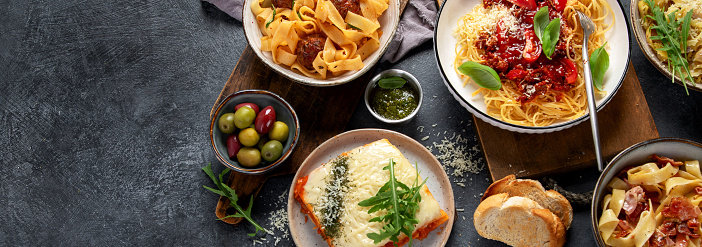 Pasta. Assortment of Italian pasta dishes, including spaghetti Bolognese, penne, tortellini, ravioli and others on a black background. Top view. Panorama with copy space.