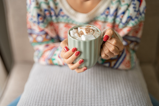 Woman holding cup of aromatic cocoa with marshmallows. Christmas eve with cup of tasty hot chocolate cozy holiday atmosphere at home.