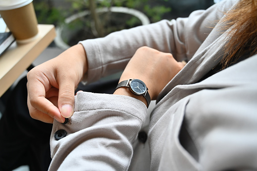 Young businesswoman buttoning up a shirt sleeve and checking time on wrist watch for appointment