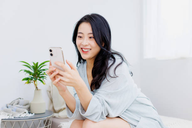 istock Happy Asian woman using her phone while sitting on her bed 1837029276