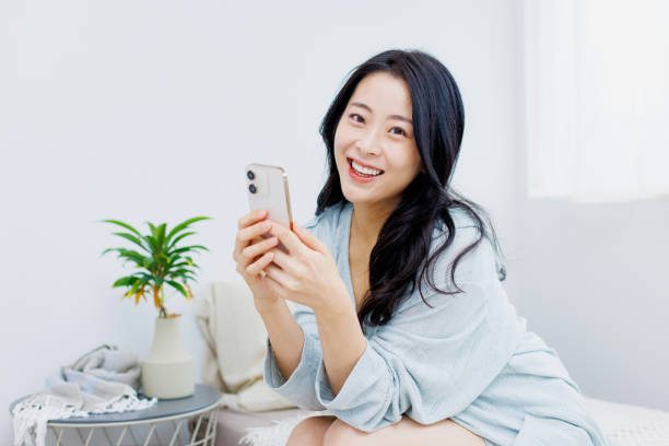 istock Happy Asian woman using her phone while sitting on her bed 1837029283