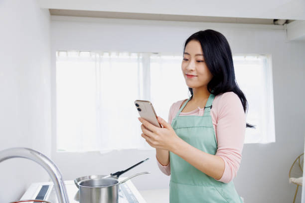 istock Asian woman using a mobile phone in the kitchen 1837033429