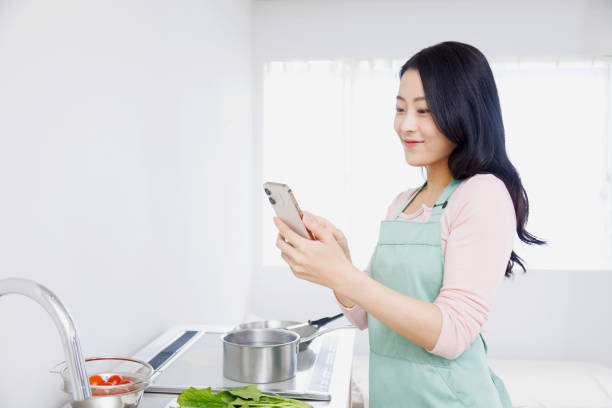 istock Asian woman using a mobile phone in the kitchen 1837033438