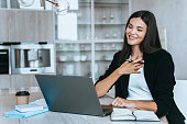 grateful young businesswoman in suit sitting at table at video call using laptop, putting hand to chest, smiling broadly, talking to business partner. distant learning student  studying via Internet