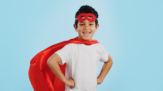 Happy, superhero or face of child with smile to fight in fantasy, dream or cosplay costume in studio. Boy power, brave or strong kid ready to protect freedom or justice with a mask on blue background