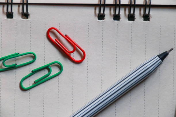 colored paperclips and pen on a paper background, Concept of different office accessories