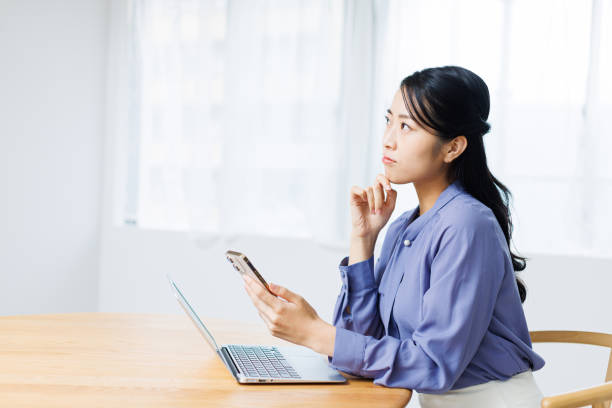 istock Young Asian woman with phone contemplating while working at home 1837098346