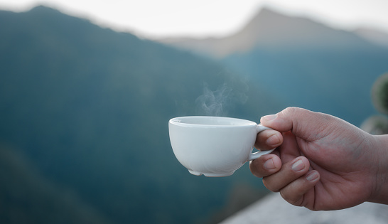hand holding a coffee cup with blurred mountain background