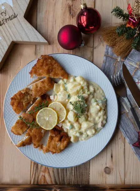 Traditional christmas eve meal for dinner or lunch with crispy and breaded chicken breast. Served with homemade potato salad on a plate on a decorated christmas table.