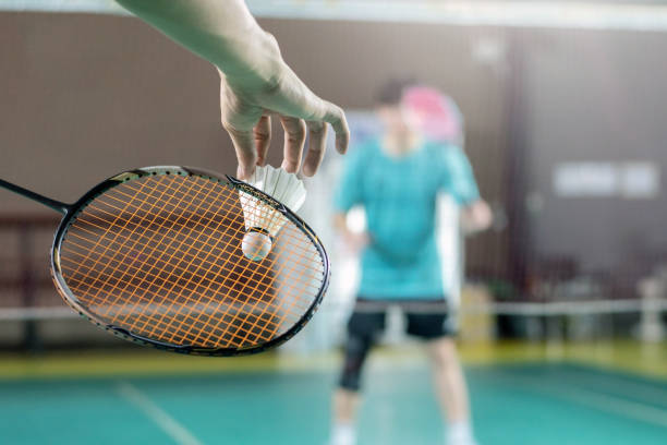 Badminton serve Badminton player holds racket and white cream shuttlecock in front of the net before serving it to another side of the court. badminton racket stock pictures, royalty-free photos & images