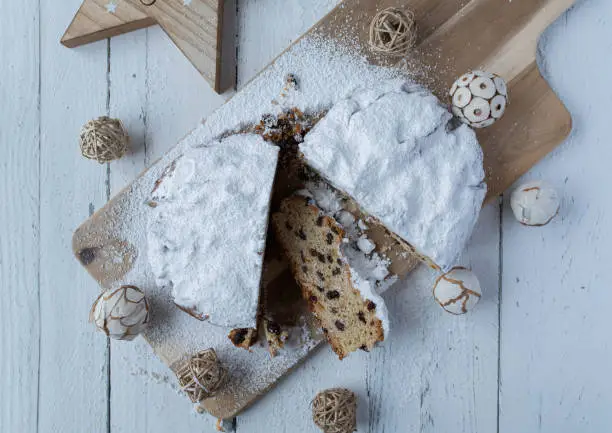Traditional dresdner Christstollen or christmas stollen from germany. Delicious fruit bread or fruitcake for advent season,   fresh and homemade baked. Served whole with cross section view on a light wooden cutting board on white table background with christmas decoration.