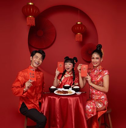 Asian family holding angpao or red packet monetary gift and dinner food for chinese new year celebration festival isolated on red decoration background. Chinese text means great luck great happy and rich.