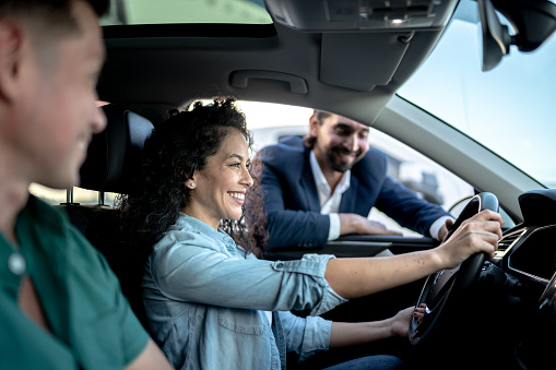 Car salesman showing a car to customer couple at dealership