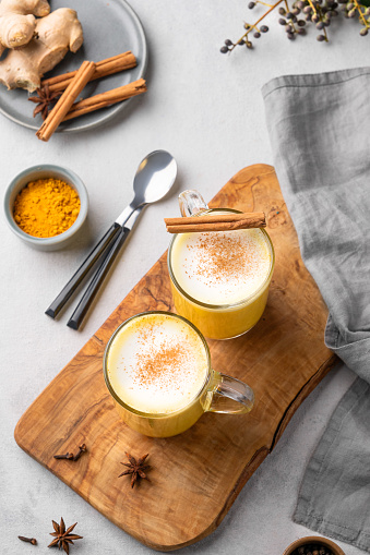 Turmeric golden milk latte with spices and honey. Detox, immunity boosting, anti-inflammatory, healthy, cozy drink in a glass cup on a wooden board on a light background. Top view.