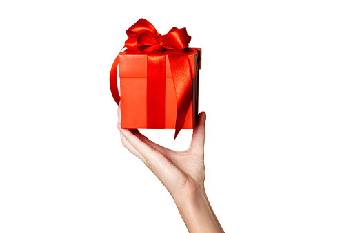 The theme of celebrations and gifts: hand holding a gift wrapped in red box with red bow isolated on white background