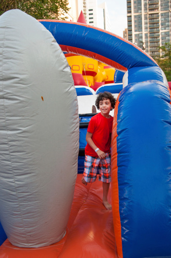 Young boy playing and having fun in an inflatable playground set in a city's neighbourhood.