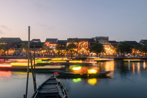 Traditional boats with lanterns in long exposure against illuminated busy waterfrost of ancient city. Old town in Hoi An, popular tourist destination in Vietnam.