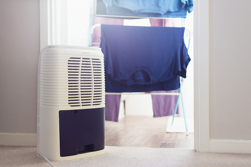 A dehumidifier next to a clothes airer with freshly laundered clothing hanging from it in a domestic room at home.