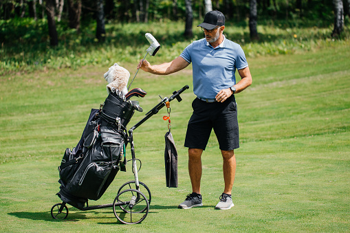 Professional older golfer takes one of clubs out of bag playing outdoors. Hand takes golf club out of bag