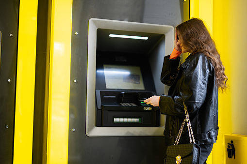 Oh no, i forgot pin code. Young disappointed brunette girl withdrawing money from credit card at yellow ATM.
