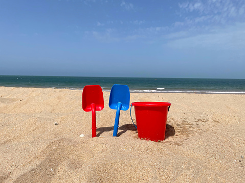 Summer sand beach concept with a red bucket and two red and blue shovels.