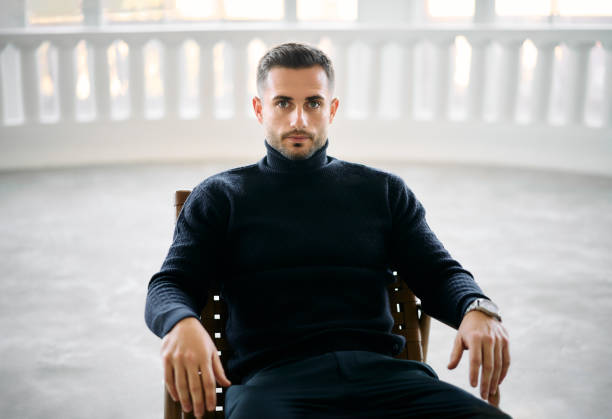 istock Handsome confident man sits in chair in modern white room with large windows 1837304359