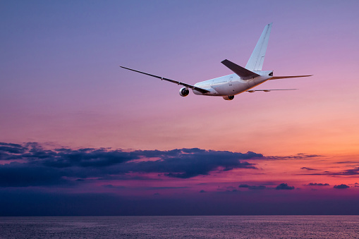 A large wide body passenger aircraft takes off over the sea against the backdrop of a picturesque sunset sky