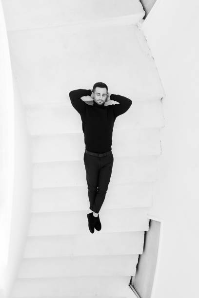 Young man in a black outfit lying on a white staircase. Top view
