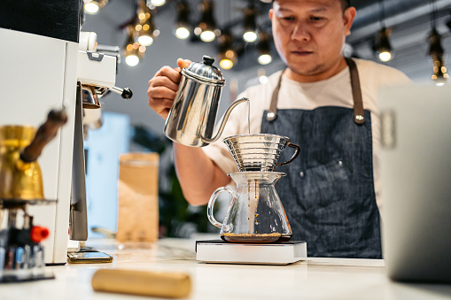 Handsome young barista making a pour-over (drip) coffee in a coffee shop in Kuwait City in Kuwait.