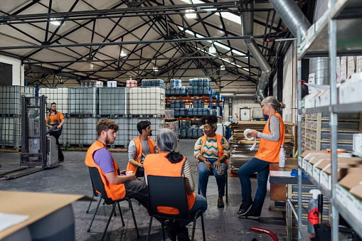 A team of five colleagues wearing casual clothing and reflective vests in a family ran ink factory in Hexham, Northeastern England. They are sat in a circle having a meeting.