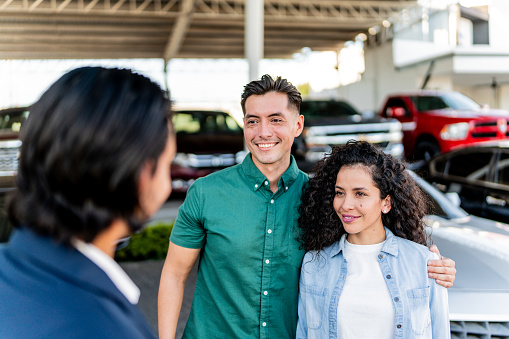 Mid adult couple talking with car salesman at dealership