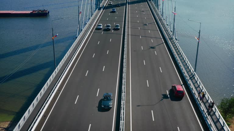 A powerful convertible driving over the bridge. Retro car surrounded by modern city cars. New road. Drone shot