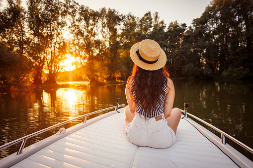 Back view of young woman relaxing while on summer vacation sailing to the sunset on a boat