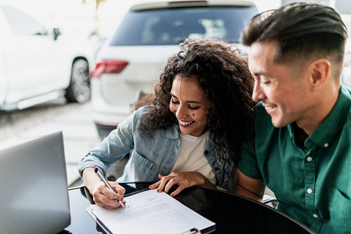 Mid adult couple signing documents to buy a car at dealership